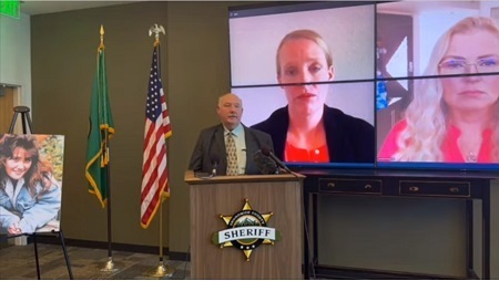 Detective Jim Scharf at the podium with Parabon's Ellen Greytak (right) and CeCe Moore (left) in the background. A photo of Michelle Koski sits to the right of Scharf.